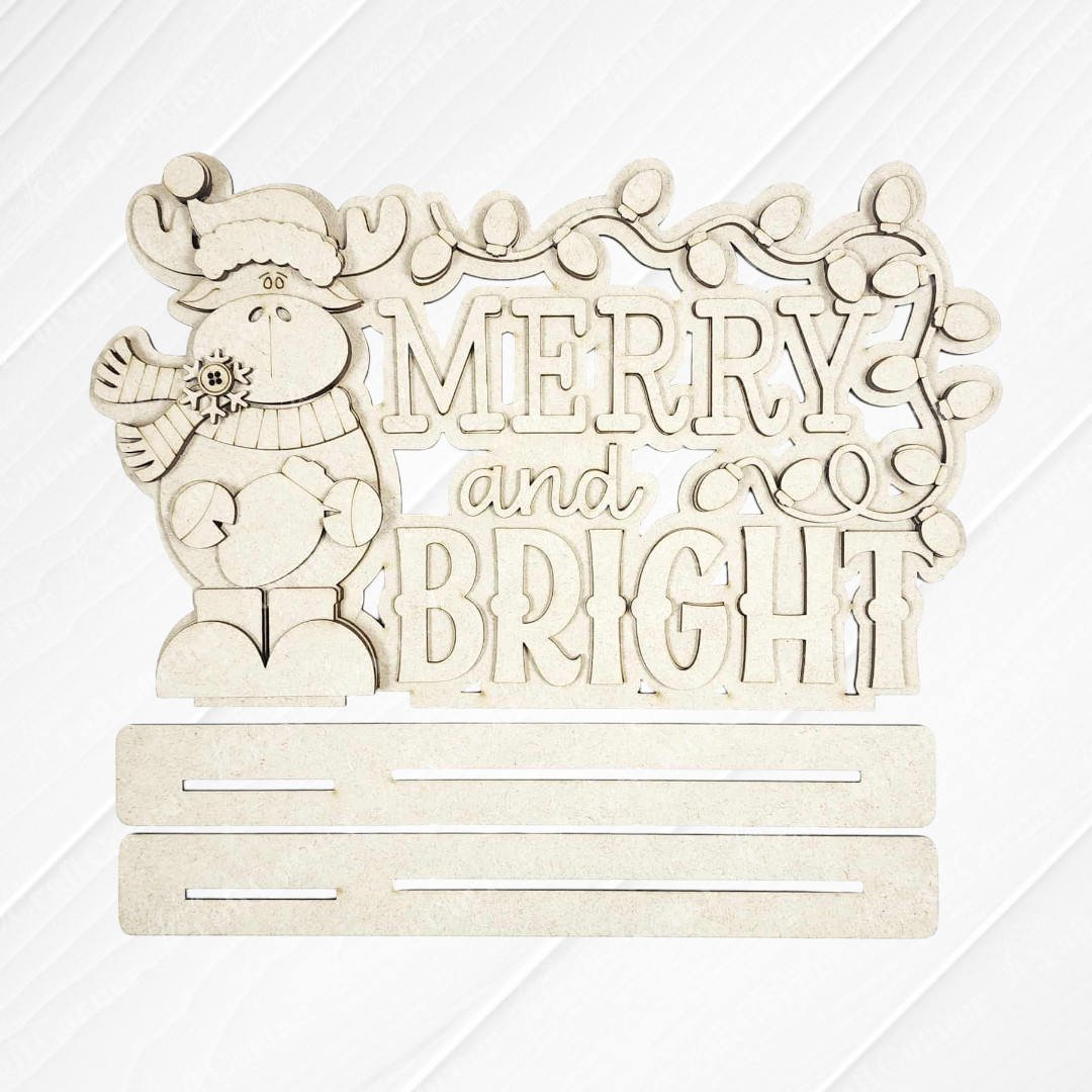 Add woodland charm to your home with Janet's Craft Corner's Moose Merry and Bright Word Art Shelf Sitter DIY kit—a festive moose in winter attire, "Merry and Bright" text, string lights above, and two slots below for display. Set of 1.