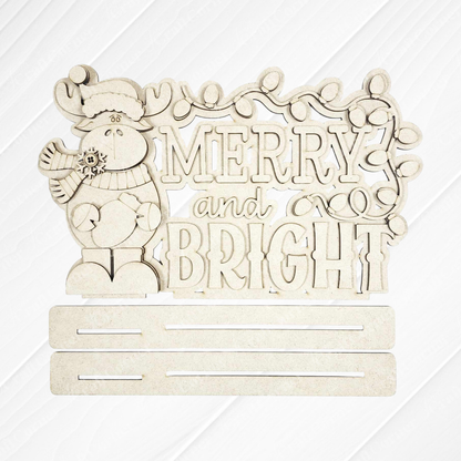 Add woodland charm to your home with Janet's Craft Corner's Moose Merry and Bright Word Art Shelf Sitter DIY kit—a festive moose in winter attire, "Merry and Bright" text, string lights above, and two slots below for display. Set of 1.