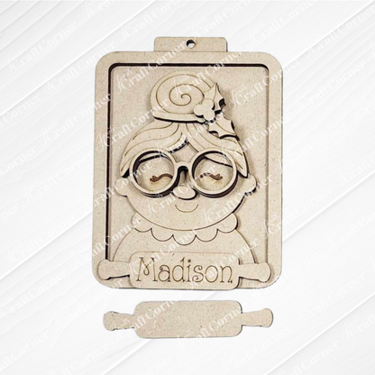 This festive Mrs. Claus ornament from Janet's Craft Corner features a cartoon grandmother with glasses and a bun, "Madison" engraved on a rolling pin, and a top hole for easy hanging with Santa ornaments on your tree.
