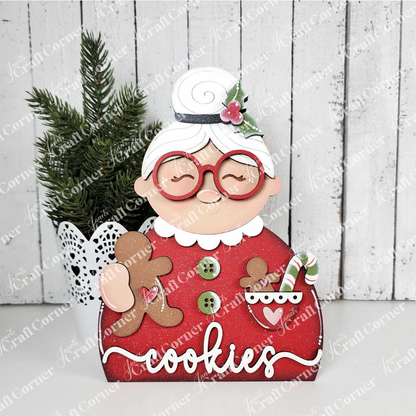 Janet's Craft Corner Mrs. Claus Shelf Sitter is a DIY seasonal home decor craft kit featuring Mrs. Claus in red glasses and dress, holding a gingerbread cookie and candy cane cup—perfect for festive holiday decorating. Set of 1.