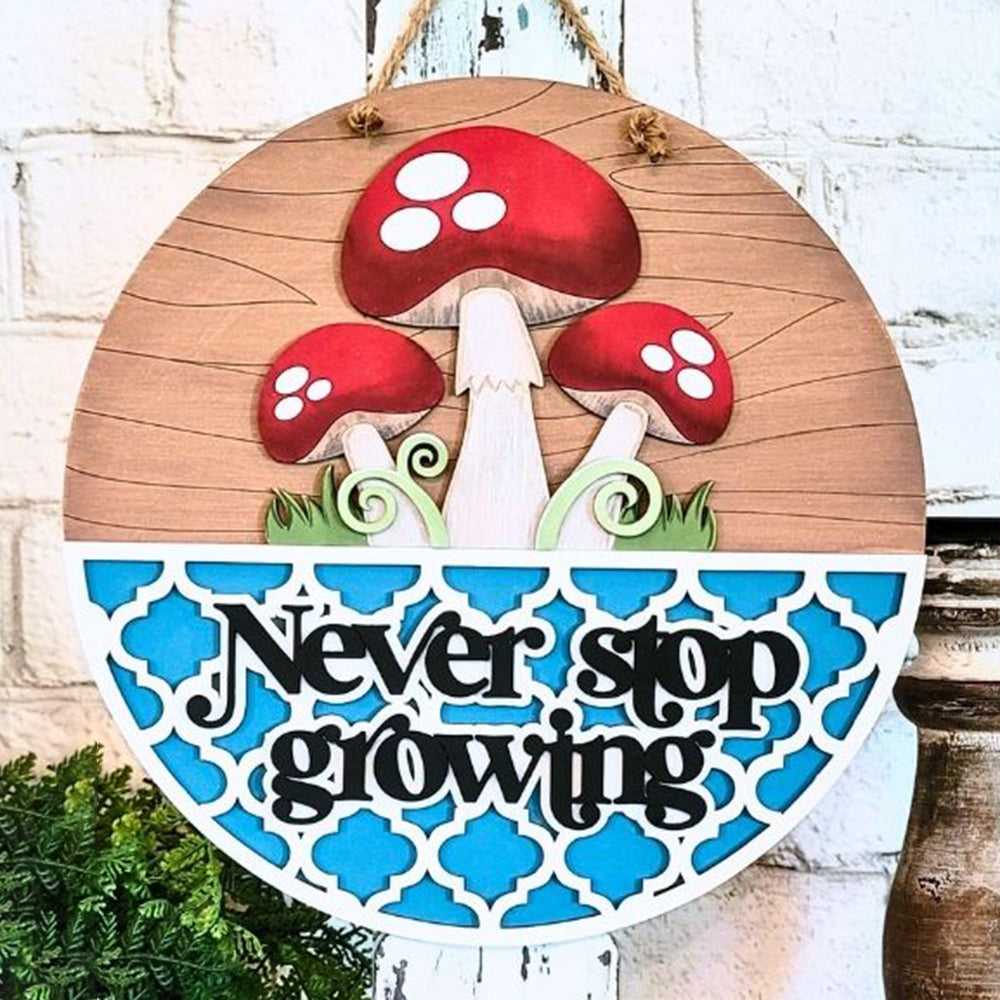 This enchanting home décor piece, the "Never Stop Growing Wall Hanger" by Janet's Craft Corner, features a charming mushroom design with three red mushrooms accented by white spots above a blue and white patterned half-circle. Below, the motivational message "Never stop growing" is set against a white brick wall highlighted by subtle greenery.