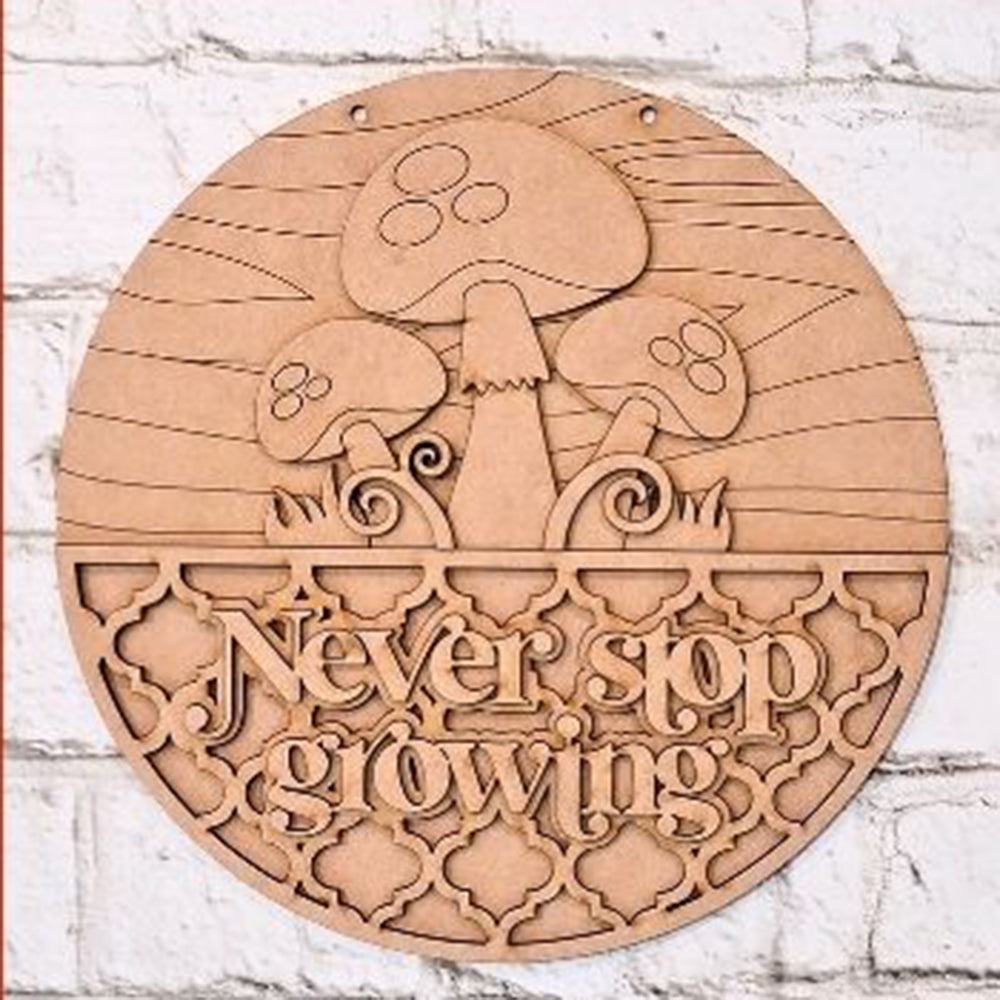 A charming round wooden sign from Janet's Craft Corner, featuring an enchanting mushroom design above the words "Never Stop Growing" in decorative script, is displayed against a brick wall. The "Never Stop Growing Wall Hanger | DIY home decor kit" is perfect for home décor enthusiasts, offering intricate patterns and DIY craft appeal to enhance any space.