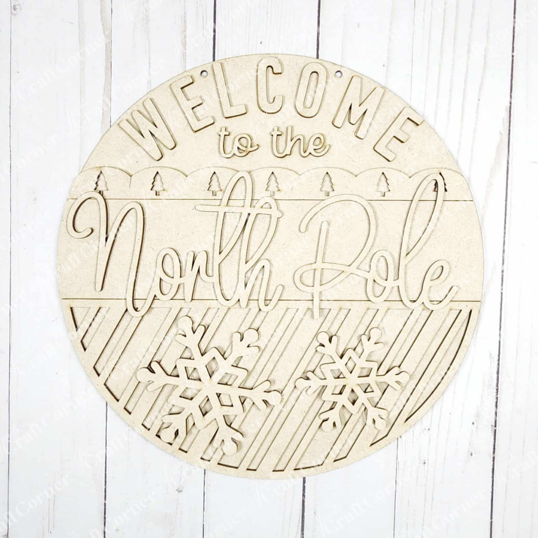 Janet's Craft Corner North Pole Door/Wall Hanger DIY kit includes a round sign with cutout "Welcome to the North Pole" letters, snowflakes, and diagonal stripes—perfect for festive seasonal home decor. Set of 1.