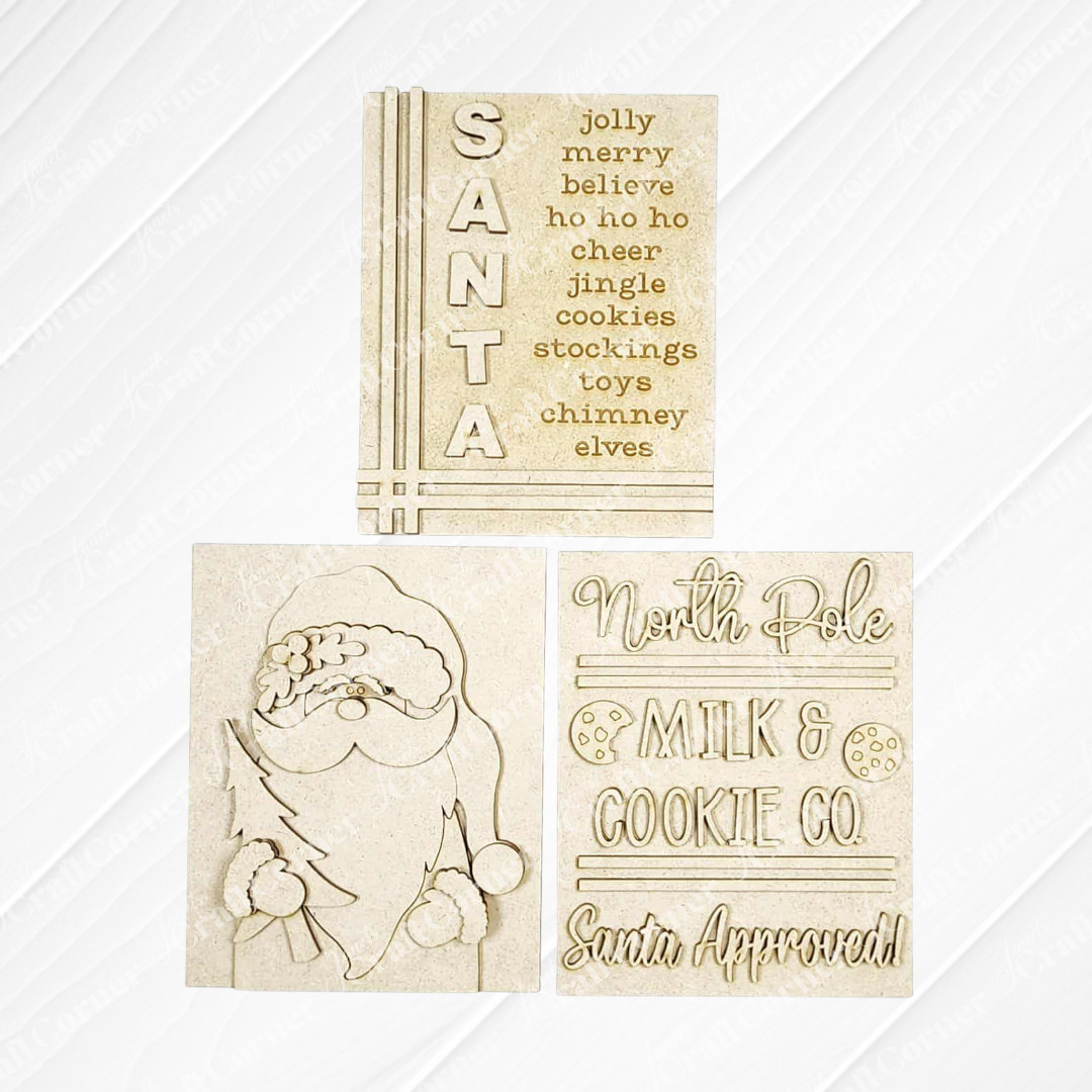 The North Pole Switchable Farmhouse Signs by Janet's Craft Corner feature three beige wood holiday signs: one with Christmas words, one with Santa Claus, and one reading "North Pole Milk & Cookie Co. Santa Approved!"—perfect festive DIY decor.