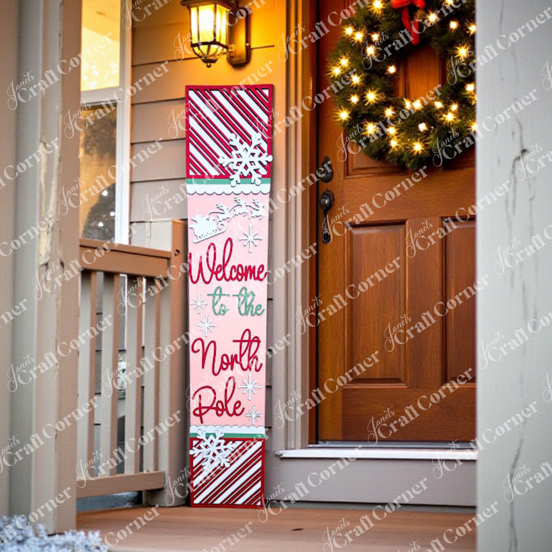A festive porch displays Janet's Craft Corner's North Pole Porch Leaner DIY seasonal home decor craft kit, surrounded by holiday touches like a wreath and string lights—creating a charming, handmade welcome for guests.