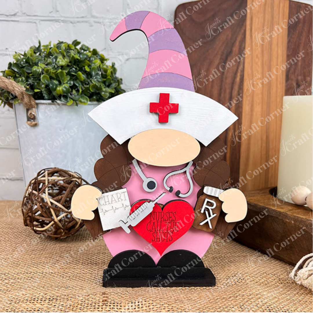 Introducing the Nurse Gnome from Janet's Craft Corner, a delightful wooden figurine featuring a pink hat and a stethoscope. This DIY kit also comes with a chart and syringe accessory. The gnome holds a red heart inscribed with "Nurses Call the Shots," making it an ideal addition to farmhouse decor. Perfectly suited for display on tabletops surrounded by decorative plants and wooden accents.