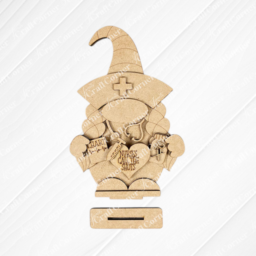 The Nurse Gnome Shelf Sitter from Janet's Craft Corner is a DIY home decor craft kit featuring a wooden cutout shaped like a nurse gnome with medical items and "Nurses Call the Shots" text, perfect for farmhouse decor against its patterned background.