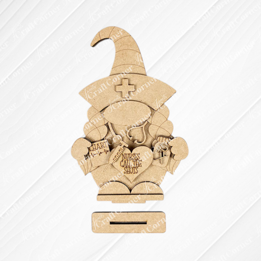 The Nurse Gnome Shelf Sitter from Janet's Craft Corner is a DIY home decor craft kit featuring a wooden cutout shaped like a nurse gnome with medical items and "Nurses Call the Shots" text, perfect for farmhouse decor against its patterned background.