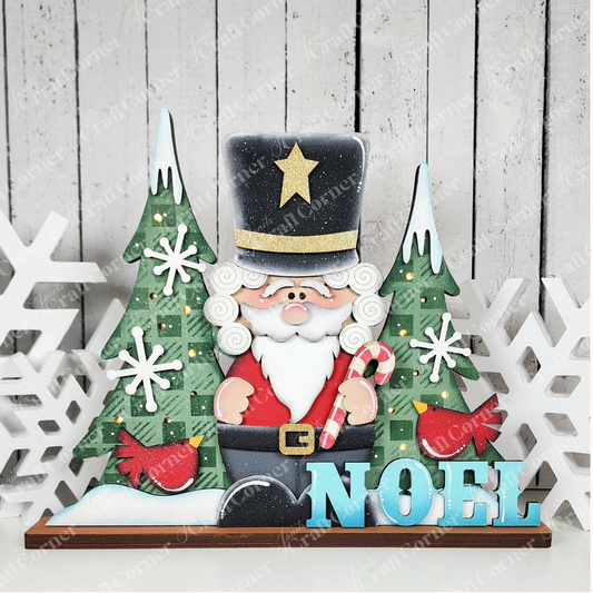 Add a festive touch to your home with this holiday décor piece, featuring Santa in a tall black hat, flanked by two Christmas trees, delicate snowflakes, and the word “NOEL” in blue letters on a rustic white wooden background—an ideal accent to display alongside your Janet’s Craft Corner Nutcracker Light-Up Shelf Sitter or pair with their DIY home decor craft kit.