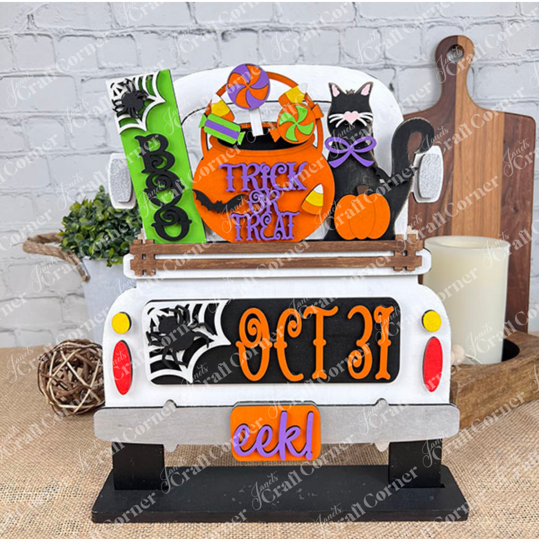 An enchanting Halloween-themed display depicts the rear of a truck adorned with vibrant signs that say "Boo," "Trick or Treat," and "Oct 31." This DIY craft kit from Janet's Craft Corner, named the Oct 31 Interchangeable Insert, features hand-painted elements including candies, a black cat with a pumpkin, and other festive decorations—ideal for creating versatile home decor.
