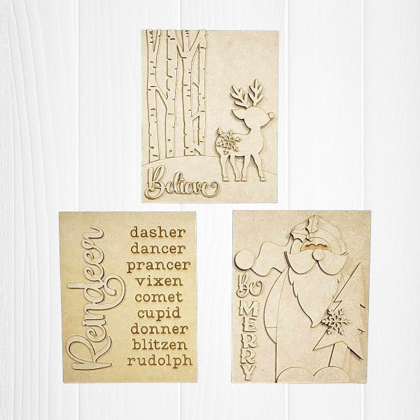 Displayed against a white plank wall this set of Oh Deer Switchable Farmhouse Signs are DIY seasonal home decor kits with a reindeer theme. One features the wood cut-out word “Reindeer” with words that evoke the fun holiday animal, another features a deer with the word “Believe” and the last features a Santa with a long beard with the words “Be Merry”.