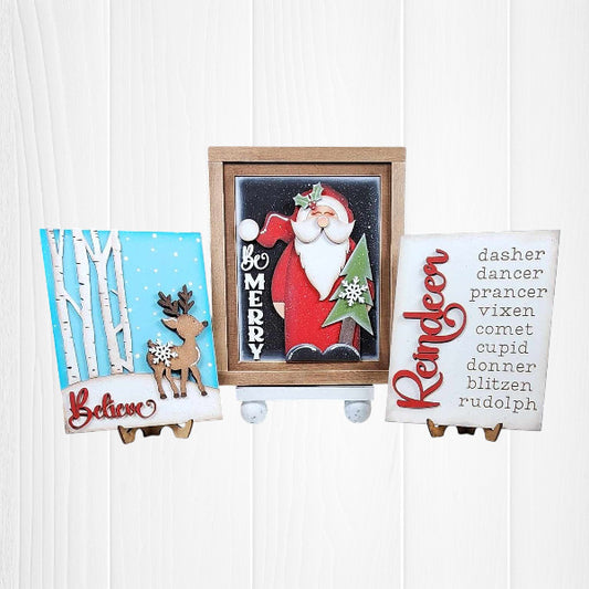 Janet's Craft Corner – Sample painted set of Oh Deer Switchable Farmhouse Signs are DIY seasonal home decor kits with a reindeer theme. One features the wood cut-out word “Reindeer” with words that evoke the fun holiday animal, another features a deer with the word “Believe” and the last features a Santa with a long beard with the words “Be Merry”.