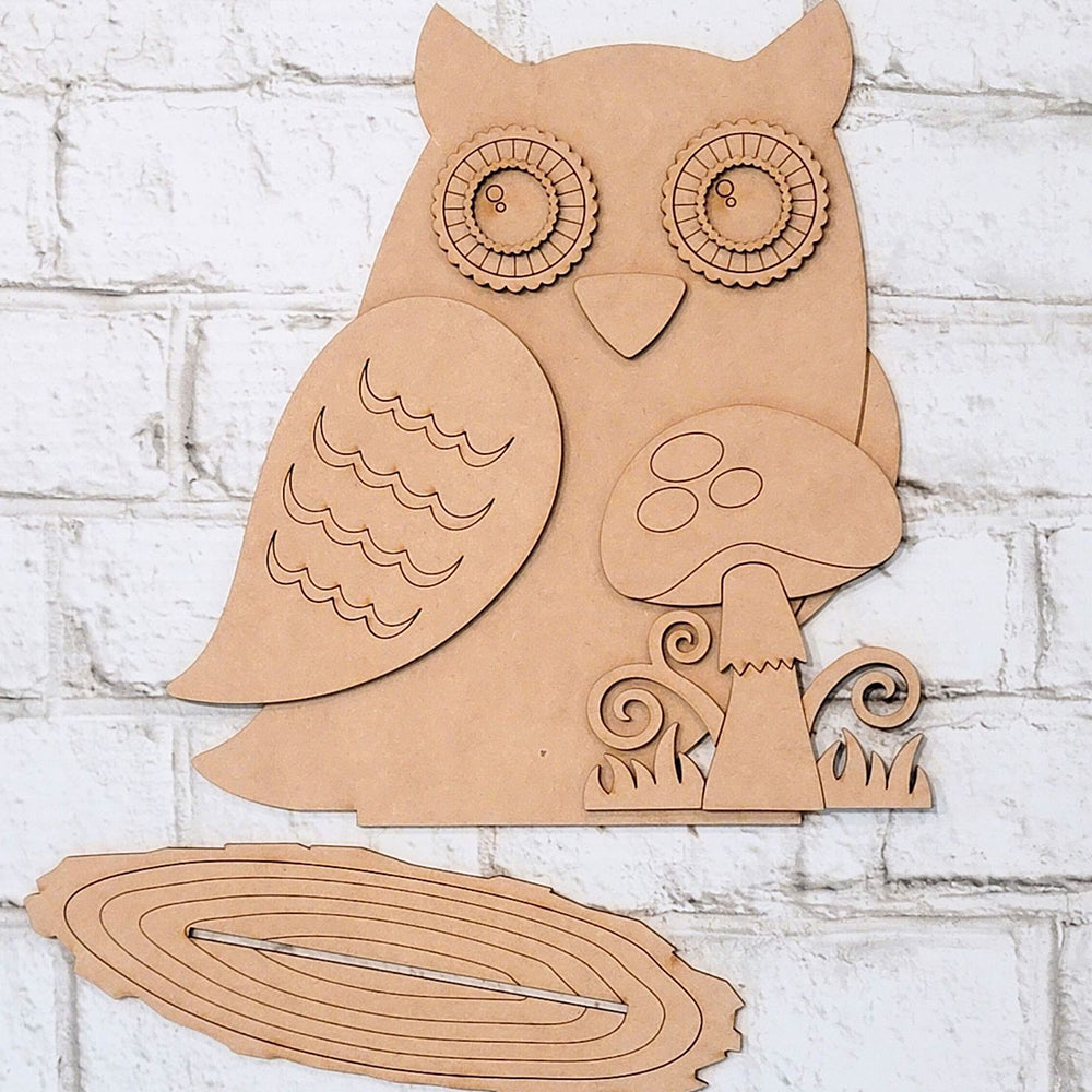 Explore the Owl with Mushroom DIY home decor kit by Janet's Craft Corner, a wooden masterpiece featuring intricate patterns, decorative swirls, and an enchanting mushroom element. Ideal for home decoration, its pieces elegantly lie on a white brick surface, encouraging creativity with every hand-painted assembly.