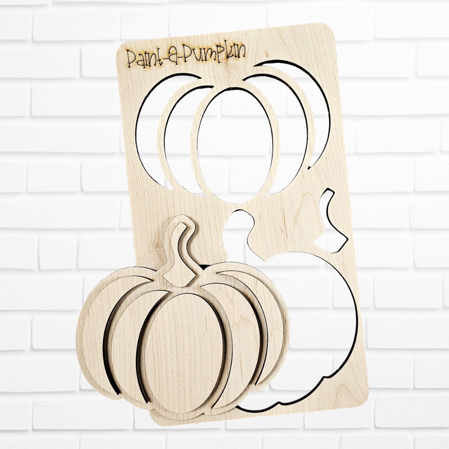 Janet's Craft Corner introduces the "Paint a Pumpkin Kids Pop-Out Kit," a perfect DIY craft set for creative enthusiasts. This home décor kit features wooden pumpkin cutouts on a white brick background with a large stencil showcasing two pumpkin shapes and matching cutout pieces below. The engraved text at the top reads "Paint a Pumpkin," inviting you to get creative.