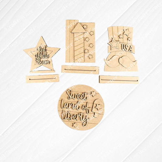 Janet's Craft Corner Patriotic Mini Shelf Sitters DIY Craft Kit includes five unfinished wood designs—star with "Red White Boom," firework, USA top hat, mustache, and circle with "Sweet land of liberty"—ready to paint or display.