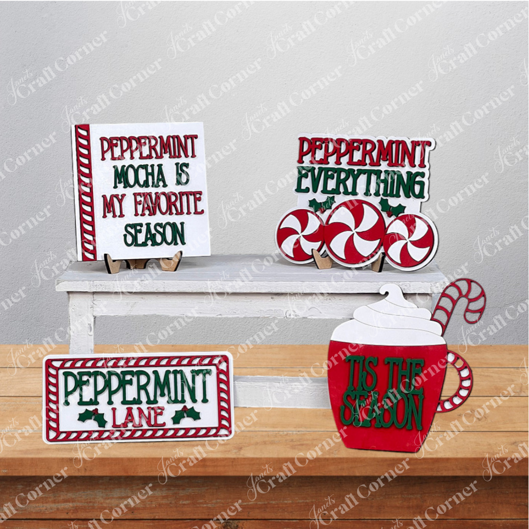 A festive arrangement featuring Janet's Craft Corner's Peppermint Mocha Tiered Tray DIY Home Decor Kit adorns your space with peppermint-themed decorations. Charming signs reading “Peppermint Mocha is My Favorite Season,” “Peppermint Everything,” and a warm greeting to “Peppermint Lane” highlight the display. The delightful red and white peppermint motifs are skillfully arranged throughout, bringing a cheerful ambiance perfect for your home décor.