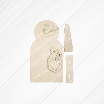 Bring a touch of winter charm to your home with the Pocket Snowman Shelf Sitter DIY craft kit by Janet’s Craft Corner. This unassembled kit includes a wooden snowman featuring a carved face, scarf, and a pocket filled with candy canes and a heart, along with two rectangular pieces—all set against a light background. Perfect for creating your own festive shelf decor!.