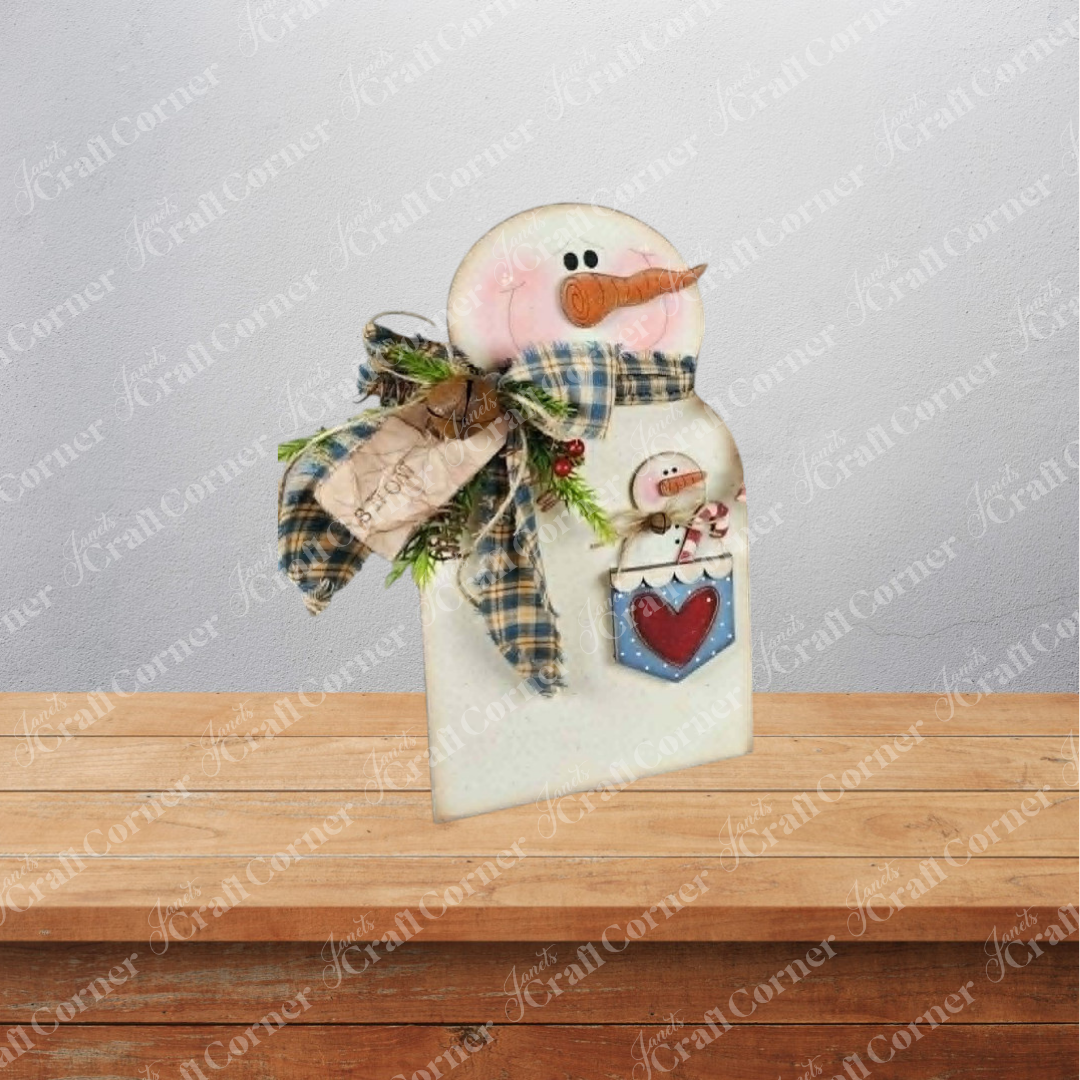 Add a touch of cozy winter charm to your home with the Pocket Snowman Shelf Sitter from Janet’s Craft Corner. This DIY home decor craft kit includes a wooden snowman figurine adorned with a plaid scarf, a wooden carrot nose, pink cheeks, and a cute tag. A pocket on the snowman features an adorable mini snowman and red heart detail. Perfect for displaying on any shelf or table, this set of 1 offers a delightful way to enhance your seasonal decor against any backdrop.
