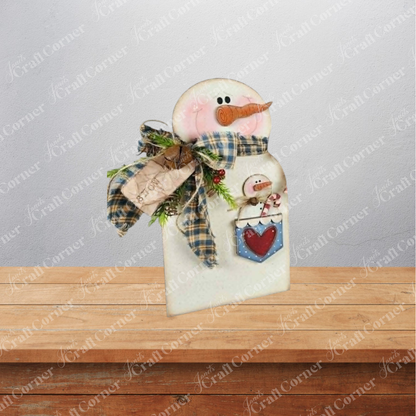 Add a touch of cozy winter charm to your home with the Pocket Snowman Shelf Sitter from Janet’s Craft Corner. This DIY home decor craft kit includes a wooden snowman figurine adorned with a plaid scarf, a wooden carrot nose, pink cheeks, and a cute tag. A pocket on the snowman features an adorable mini snowman and red heart detail. Perfect for displaying on any shelf or table, this set of 1 offers a delightful way to enhance your seasonal decor against any backdrop.