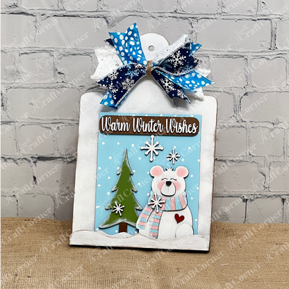 Janet's Craft Corner Breadboard Sign Holder DIY Kit includes a switchable farmhouse sign featuring a polar bear in a scarf, snowy tree, snowflakes, "Warm Winter Wishes" text, and a blue and white bow—perfect DIY home décor.