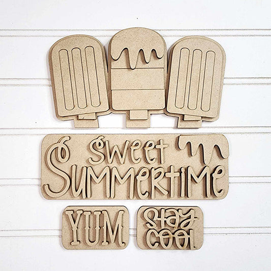 Wooden cutouts of three popsicles, decorated with phrases such as "Sweet Summertime," "Yum," and "Stay Cool" in fun, wavy fonts on a white background. This DIY home decor kit from Janet's Craft Corner is perfect for creating delightful decorations or an enchanting interchangeable insert.