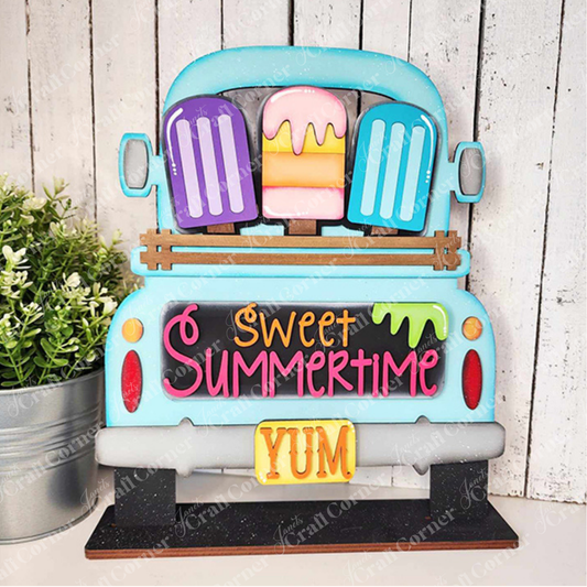 Add a charming touch to your home décor with Janet's Craft Corner's DIY home decor kit, featuring the Popsicle Interchangeable Insert. This decorative piece showcases a blue truck with vibrant popsicles and "Sweet Summertime" elegantly written in pink and orange above a yellow "YUM" license plate. It’s perfect for placing next to a potted plant on a wooden surface.