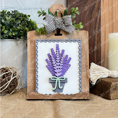 The Lavender Switchable Farmhouse Signs DIY Craft Kit from Janet's Craft Corner features a decorative wooden clipboard with 3D paper lavender flowers in a pot, tied with a green bow and finished with a black-and-white striped ribbon for tabletop decor.