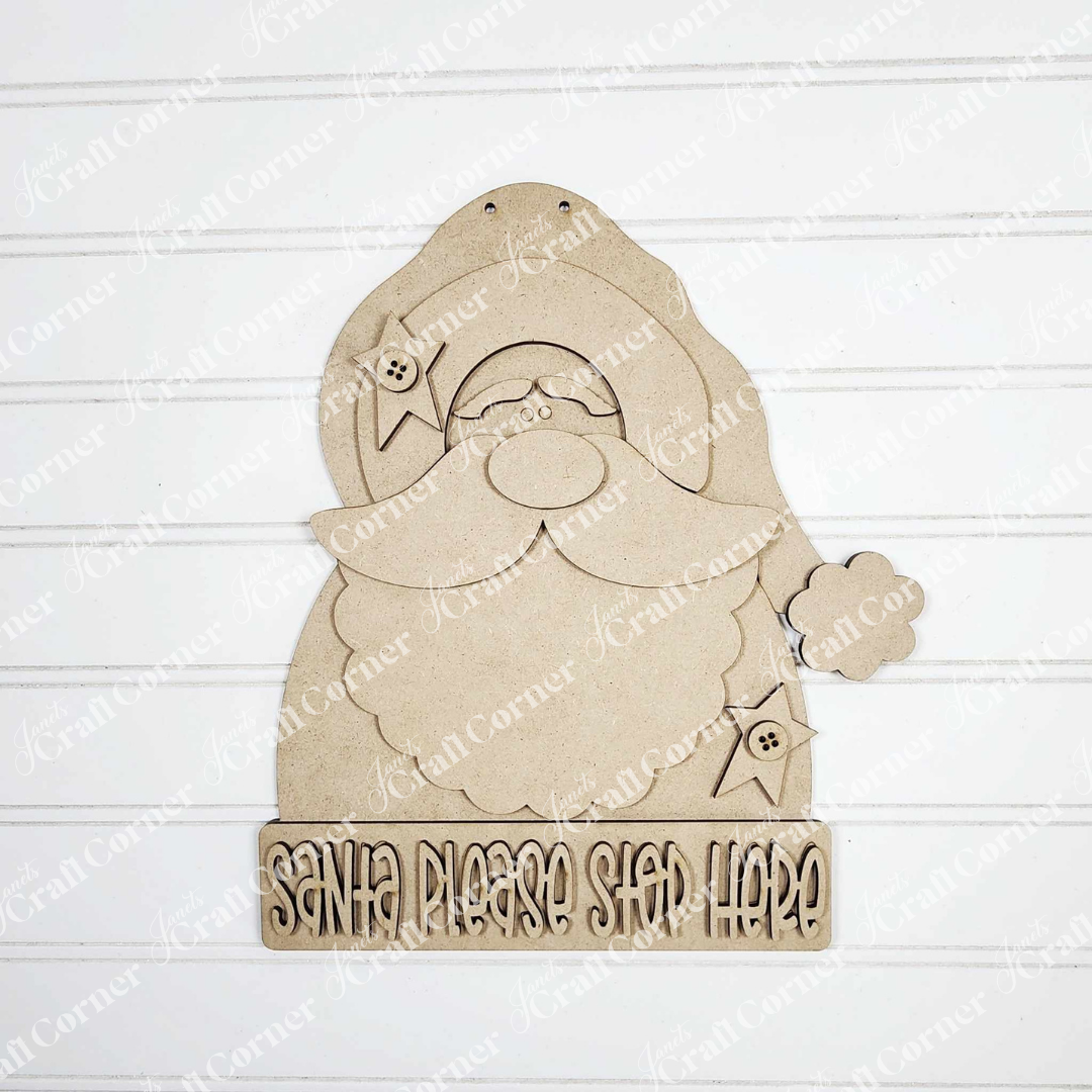 The Primative Santa Door Hanger by Janet's Craft Corner features a wooden Santa with a "Santa Please Stop Here" sign, perfect as festive home decor against white shiplap.
