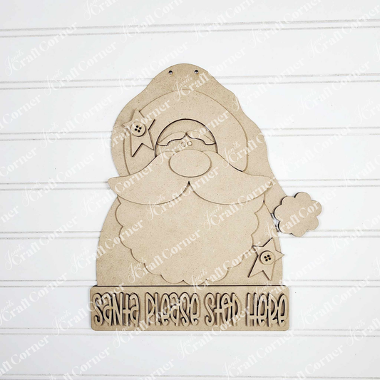 The Primative Santa Door Hanger by Janet's Craft Corner features a wooden Santa with a "Santa Please Stop Here" sign, perfect as festive home decor against white shiplap.