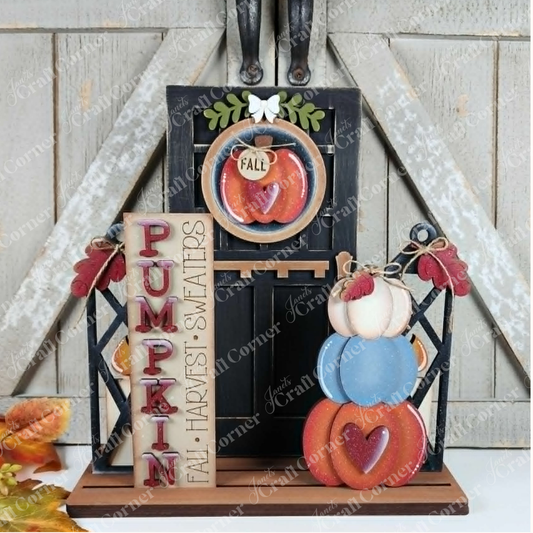 Bring seasonal charm to your porch with Janet’s Craft Corner Pumpkin Interchangeable Porch Set—a DIY home decor craft kit featuring 5 pieces, including stacked pumpkins, a “PUMPKIN” sign, and a “FALL” mug. Accented with autumn leaves and hearts in front of rustic barn doors, it’s the perfect pumpkin porch decor for fall harvest decorations.