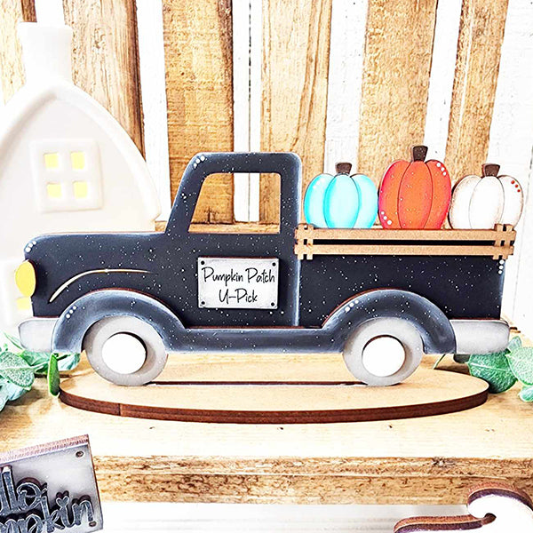 The "Pumpkin Truck Mini Shelf Sitter" DIY home decor kit by Janet's Craft Corner includes a decorative wooden board shaped like a vintage truck with a charming pumpkin design, featuring the sign "Pumpkin Patch U-Pick." The truck bed is filled with pastel-colored pumpkins and is showcased against a rustic wooden background, complete with a small white house decoration.