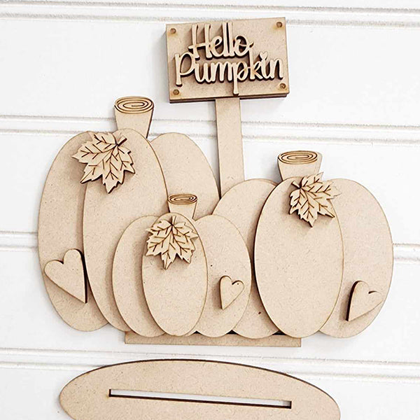 This charming decor piece by Janet's Craft Corner, named the Pumpkins Mini Shelf Sitter, features five wooden pumpkin shapes adorned with three-dimensional leaf and heart cutouts. It includes a small rectangular sign that says "Hello pumpkin" and can be used as part of a DIY home decor kit for added creativity.