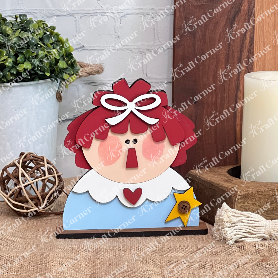 The Raggedy Ann & Andy Shelf Sitter from Janet's Craft Corner features red hair, a blue dress, and yellow star—perfect for seasonal decor or as a DIY craft kit. Set of 1; display on tables or shelves to add charm to your home.