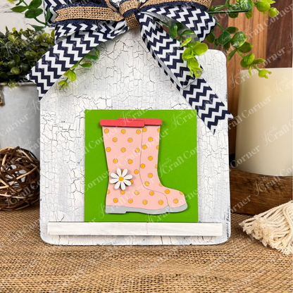 Janet's Craft Corner Hello Spring Squares features a pink rain boot with yellow polka dots and a white daisy on a green square, set on rustic wood with greenery accents and a chevron bow—ideal for tiered trays or Swappable Squares decor.