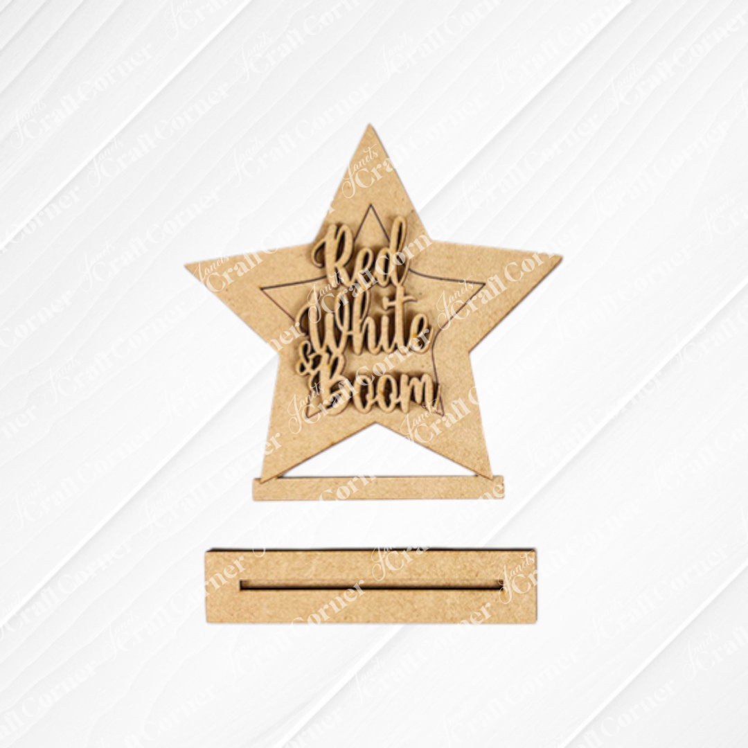 Janet's Craft Corner Patriotic Mini Shelf Sitters – DIY Craft Kit includes a wooden star with "Red, White & Boom" cutout, perfect for Americana décor. It stands upright on a textured white base.