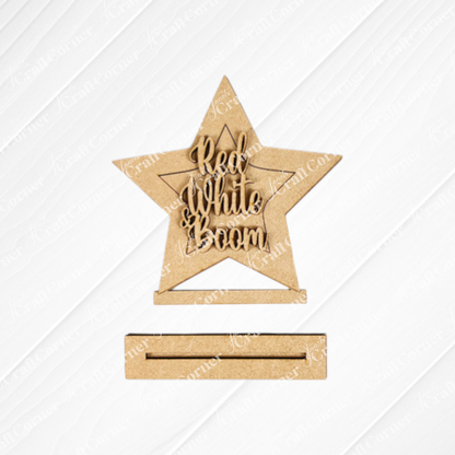 Janet's Craft Corner Patriotic Mini Shelf Sitters – DIY Craft Kit includes a wooden star with "Red, White & Boom" cutout, perfect for Americana décor. It stands upright on a textured white base.