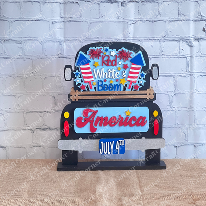 Janet's Craft Corner offers a "Red White & Boom Interchangeable Insert" featuring a patriotic black truck with fireworks and the phrases "Red White & Boom" and "America Land that I Love," plus a "July 4th" license plate, all on a white brick background—perfect for DIY seasonal home decor.