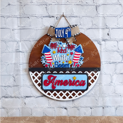 The Janet's Craft Corner "Red White & Boom" Interchangeable Insert is a DIY home decor piece featuring "July 4th" on a small sign and "Red, White, & Boom" with fireworks on the main sign. Below, it states "America and that I love," set against a lattice background with a white brick wall backdrop.