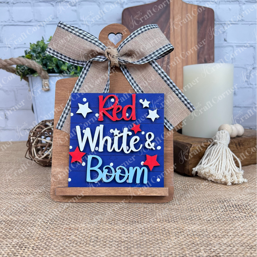Janet's Craft Corner Patriotic Squares DIY kit includes a decorative wooden sign with a plaid bow and "Red, White & Boom" in red, white & blue. Perfect Independence Day décor—kit comes with an easel, candle, and tassel accents.