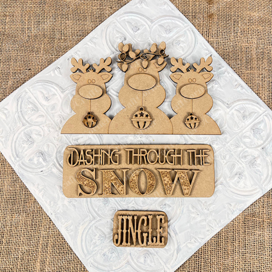 The Reindeer Interchangeable Insert from Janet's Craft Corner features three antlered reindeer set against a textured burlap background, with signs that read "Dashing Through the Snow" and "Jingle." As a DIY home decor kit, it is perfect for adding festive charm to any space.
