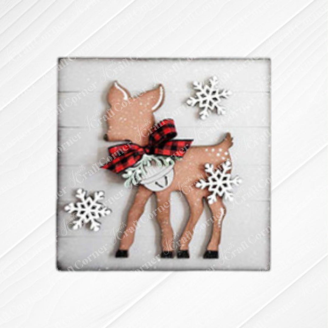 The Mistletoe Swappable Squares DIY craft kit from Janet's Craft Corner lets you create seasonal home decor—choose from 4 designs, including wood cut-outs perfect for tiered tray displays on a white wooden background.
