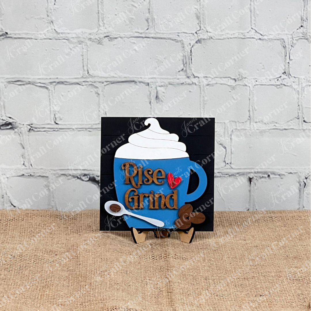 The Coffee Swappable Squares DIY seasonal home decor craft kit by Janet's Craft Corner features a blue coffee mug sign with whipped cream, "Rise & Grind" text, and a red heart—perfect decor for coffee lovers.