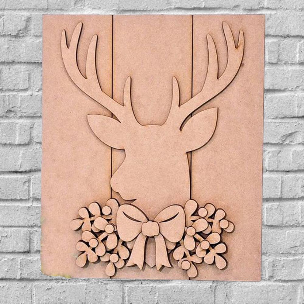 The Rustic Deer Shelf Leaner DIY Home Decor Kit by Janet's Craft Corner is perfect for festive decoration. It showcases a silhouette of a deer’s head with antlers, complemented by a decorative bow and floral design below. The light brick wall background adds to its charming appeal.