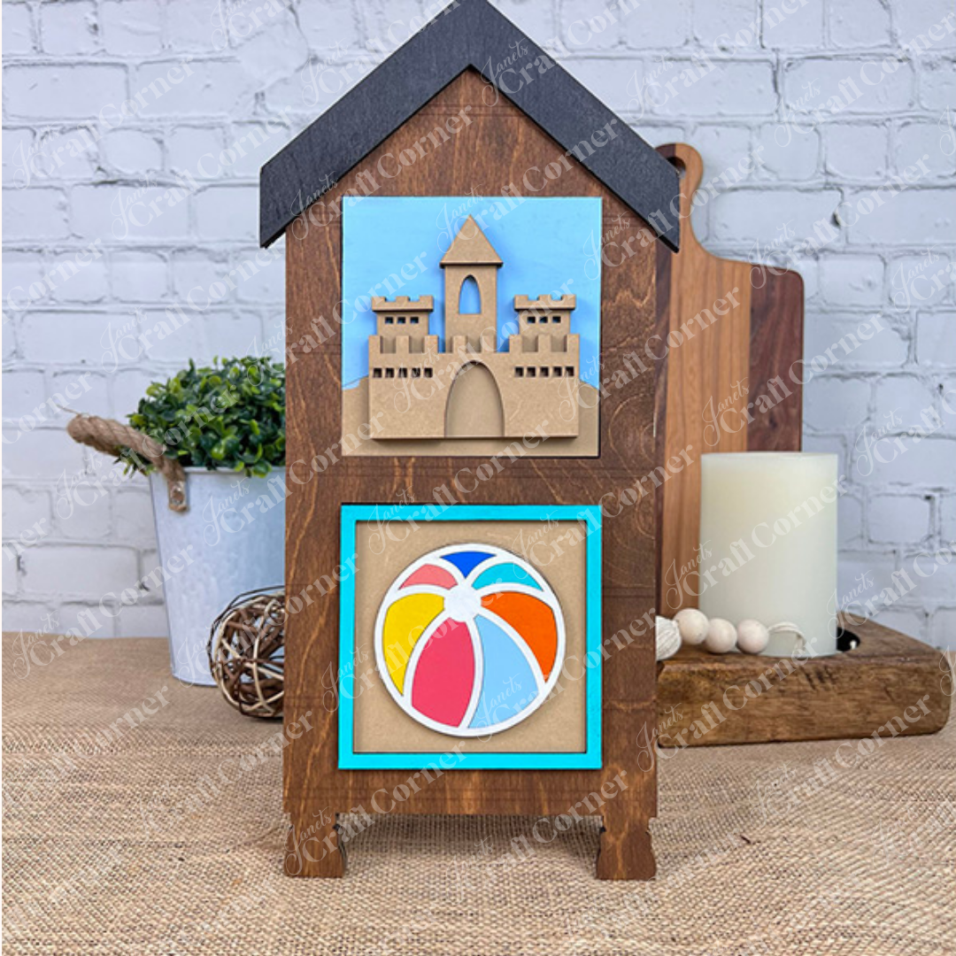 The Summer Beach Squares DIY craft kit by Janet's Craft Corner includes a wood house cut-out with a layered sandcastle and beach ball design, perfect for summer tiered tray or coffee bar decor.