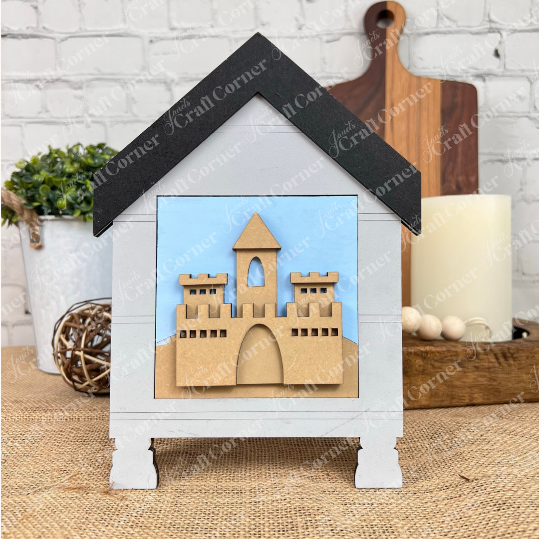 The Summer Beach Squares DIY seasonal home decor craft kit from Janet's Craft Corner includes a small decorative wood frame with layered beach cut-outs on a blue background, perfect for tiered trays. Display it with plants and candles for a charming touch.