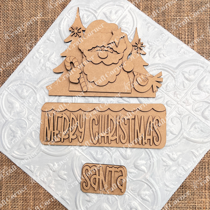 Janet's Craft Corner Santa Merry Christmas Interchangeable Insert DIY kit includes 3 laser-cut wooden pieces—Santa, trees, sweets—with "Merry Christmas." Perfect for seasonal crafts. Displayed on a white embossed tile and burlap background.
