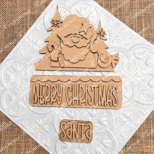 Janet's Craft Corner Santa Merry Christmas Interchangeable Insert DIY kit includes 3 laser-cut wooden pieces—Santa, trees, sweets—with "Merry Christmas." Perfect for seasonal crafts. Displayed on a white embossed tile and burlap background.