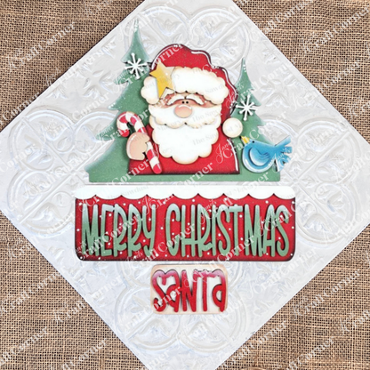 Janet's Craft Corner Santa Merry Christmas Interchangeable Insert DIY kit features a smiling Santa with a candy cane, vibrant "Merry Christmas" lettering, and festive trees—perfect for seasonal home decor and holiday crafts. Set includes 3 pieces.