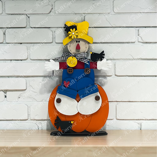 Bring cozy autumn vibes to your space with Janet’s Craft Corner Scarecrow Pumpkin Shelf Sitter—a DIY home decor craft kit featuring a charming scarecrow with a yellow hat, blue overalls, and a “Fall” tag sitting on an orange pumpkin. Perfect for displaying on shelves against a white brick wall and adding festive fall décor to your home.