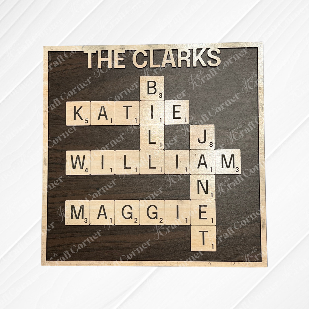 Janet's Craft Corner's Scrabble Board Sign is a personalized wooden name sign featuring "THE CLARKS" and the names KATIE, BILL, WILLIAM, MAGGIE, and JANET in a crossword—an ideal engraved wood décor for families.